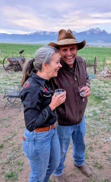 Couple laughing together with drinks at the Cadillac Wanch, Sangre de Cristo mountains in the background
