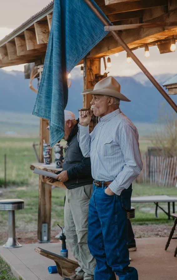 Cowboy in hat enjoying a cigar under the covered structure at Turkey Toe with the Sangre de Cristo mountains at dusk