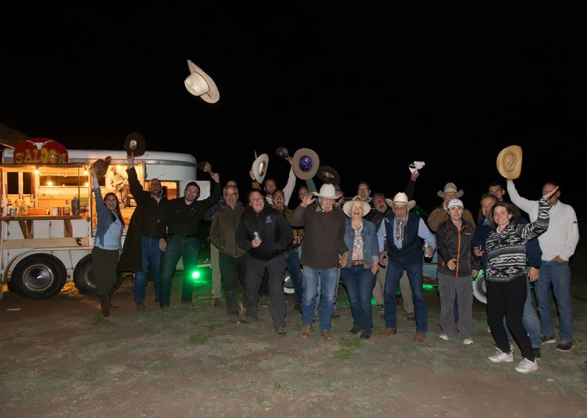 Large group throwing cowboy hats in the air celebrating in front of the Cadillac Wanch saloon at night