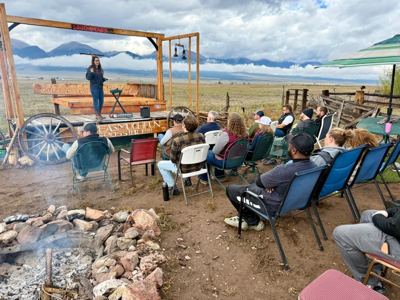 MVWD team building event with the group gathered at the Loud Guitars stage by the fire pit, Sangre de Cristo mountains in the background