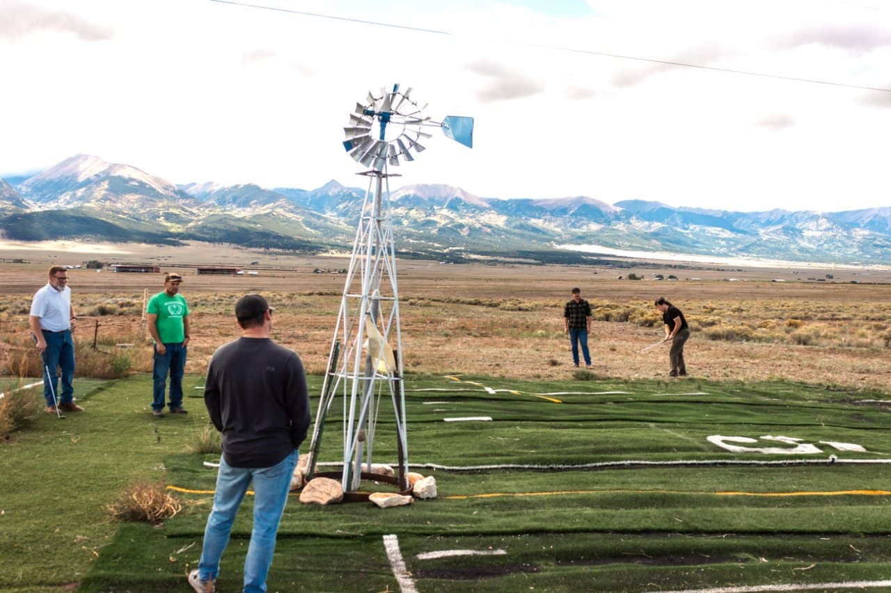 Group watching a tee shot at the windmill tee box, Sangre de Cristo mountains in the background
