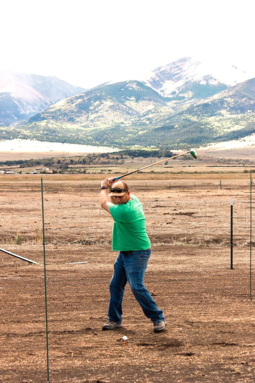 Golfer mid-swing with snow-capped Sangre de Cristo peaks in the background