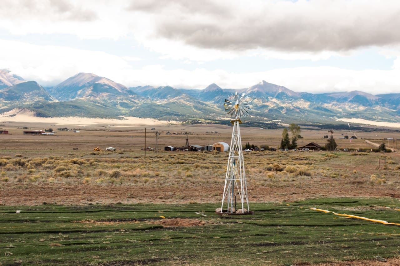 Custom windmill marker with fresh turf rows in the foreground and the Sangre de Cristo range behind