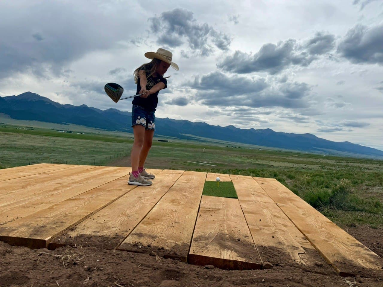 Eva teeing off at The Summit #10 tee box — custom plank tee box with Sangre de Cristo mountain views, Turkey Toe Ranch
