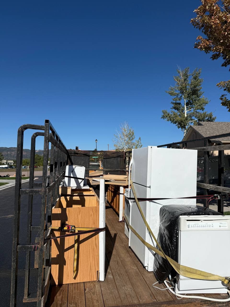 Trailer loaded with refrigerator, dishwasher, cabinets, and countertop pieces strapped down for transport