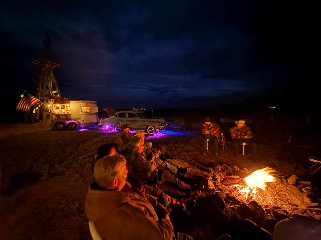 Campfire at night with live guitars — the Cadillac Wanch lit up behind